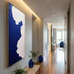 Abstract hand-painted canvas with deep indigo background and white textured shoreline, contemporary hallway