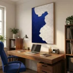 Textured abstract hand-painted canvas in deep indigo and cream with organic wave-like forms, contemporary office setting