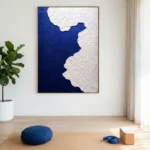 Minimalist hand-painted canvas with textured white coastline against deep navy blue, contemporary studio space