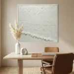 Minimalist textured hand-painted canvas depicting serene coastal landscape in soft whites and grays, styled in contemporary workspace