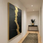 Textured abstract hand-painted canvas with striking gold leaf accent down charcoal black ground, contemporary hallway