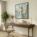 Gestural hand-painted canvas depicting an ethereal angel figure with expansive wings in cream and gold tones against soft blue, contemporary workspace