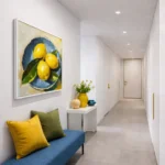 Contemporary still life hand-painted canvas depicting three golden lemons on blue plate, warm yellow and sage palette, modern hallway setting