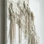Textured abstract hand-painted canvas with layered cream and ivory tones, organic sculptural fringe details, contemporary white wall
