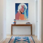 Contemporary figurative hand-painted canvas of woman with white hair in vibrant coral, blue and mint tones, entryway setting