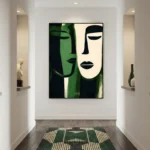 Minimalist figurative hand-painted canvas depicting two stylized faces in cream and forest green, contemporary hallway setting