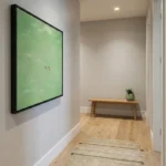 Minimalist hand-painted canvas depicting two figures on soft sage green field, contemporary hallway