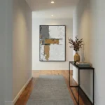 Textured abstract hand-painted canvas with gestural gold and cream brushstrokes on white, contemporary hallway