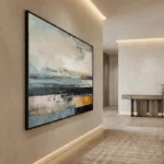 Layered abstract landscape hand-painted canvas in muted blues, creams, and ochre with gestural horizontal brushstrokes, contemporary hallway setting