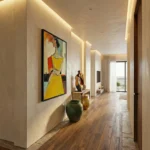 Figurative hand-painted canvas depicting woman in vibrant yellow dress with red accents, ochre and muted earth tones, modern hallway setting