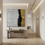 Textured abstract hand-painted canvas in white, black, and gold leaf with bold vertical division, modern hallway