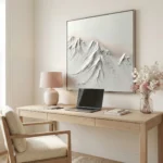 Textured monochrome hand-painted canvas depicting snow-capped mountain peaks in layered white and grey tones, contemporary workspace