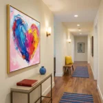 Gestural abstract hand-painted canvas in vibrant pink, blue, and yellow brushstrokes forming a dynamic heart composition, modern hallway