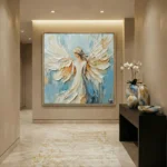 Textured figurative hand-painted canvas depicting a winged angel in cream and gold brushstrokes against soft blue, modern entryway