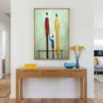 Contemporary figurative hand-painted canvas depicting stylized figures in red, yellow and blue tones, modern entryway
