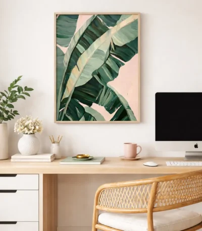 Contemporary botanical hand-painted canvas depicting layered banana leaves in deep greens and soft pinks, modern workspace