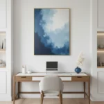 Layered abstract hand-painted canvas depicting dramatic cloudy sky in deep blues and whites, contemporary workspace