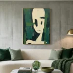 Minimalist figurative hand-painted canvas with cream face and bold black features against layered green tones, contemporary living space