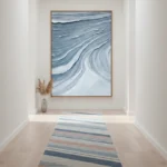 Layered abstract hand-painted canvas depicting flowing waves in deep blues and whites with gestural brushstrokes, contemporary hallway setting