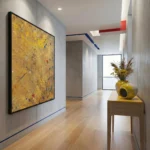 Gestural abstract expressionist hand-painted canvas in golden yellow with scattered colorful accents, modern hallway