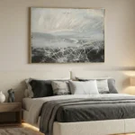 Gestural abstract hand-painted canvas layered with white expressive marks over moody landscape in grays and blacks, modern bedroom setting