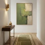 Layered abstract hand-painted canvas in soft greens, creams, and ochre with geometric composition, contemporary hallway