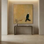 Minimalist hand-painted canvas depicting a figure in motion with a small dog and delicate branches against warm ochre tones, contemporary entryway