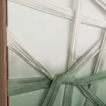 Minimalist hand-painted canvas with woven ribbon motifs in sage green and cream, contemporary interior setting