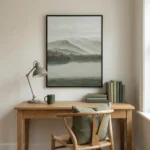 Minimalist landscape hand-painted canvas depicting misty mountains and serene water in muted greens and grays, contemporary workspace