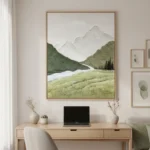 Contemporary landscape hand-painted canvas depicting snow-capped mountains, forested valleys, and a meandering river in muted greens and whites, modern workspace