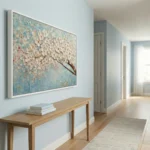 Textured hand-painted canvas depicting delicate white blossoms on brown branch with blue-green background, contemporary hallway