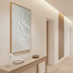 Textured abstract hand-painted canvas with layered white and cream tones depicting organic wave forms, contemporary hallway